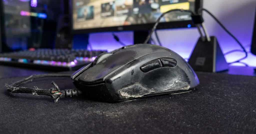 A close-up view of a heavily used gaming mouse showing worn skates, faded coating, and physical wear that can affect tracking, comfort, and reliability during FPS gaming.