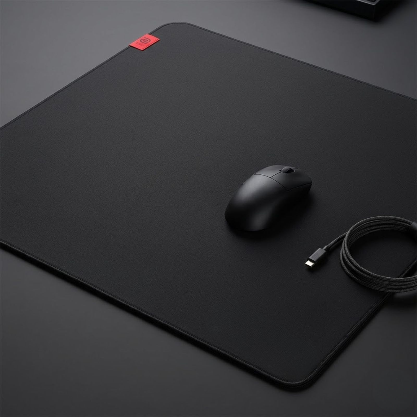 A black BenQ ZOWIE G-SR III gaming mouse pad placed on a gaming desk with a gaming mouse positioned near the center of the surface.