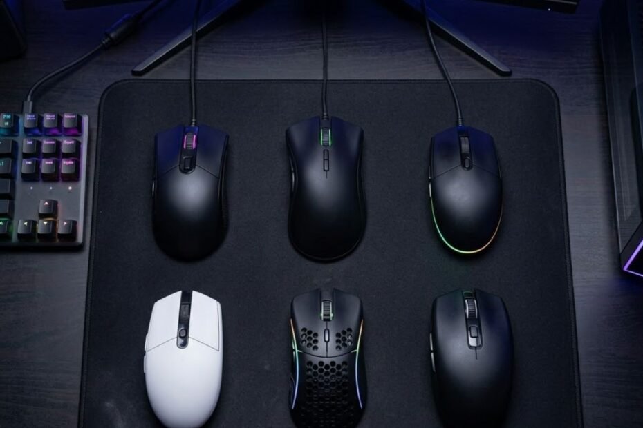 Six budget gaming mice displayed on a gaming desk beside a large mouse pad and mechanical keyboard for FPS gaming