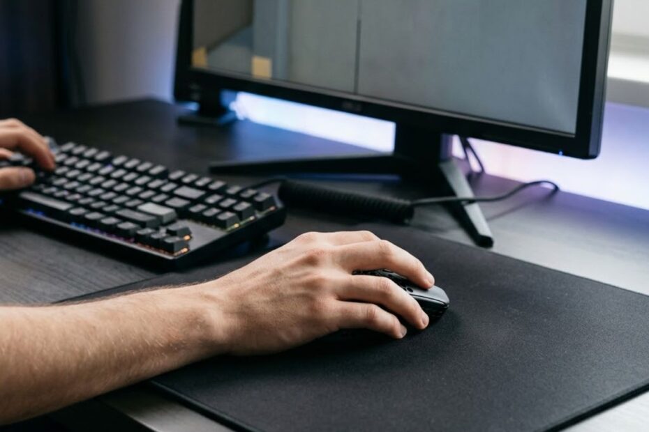 An FPS player using a gaming mouse on a large cloth mouse pad while aiming at targets on a gaming monitor, illustrating how mouse pad surfaces affect aiming consistency.