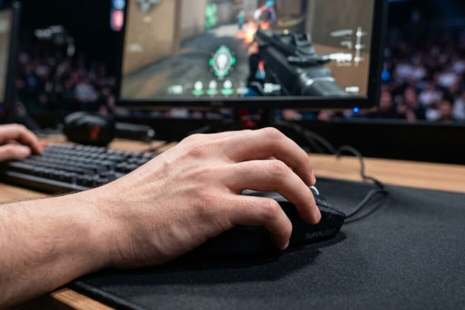 A gamer holding a gaming mouse using a claw grip with curved fingers and partial palm contact during an FPS game