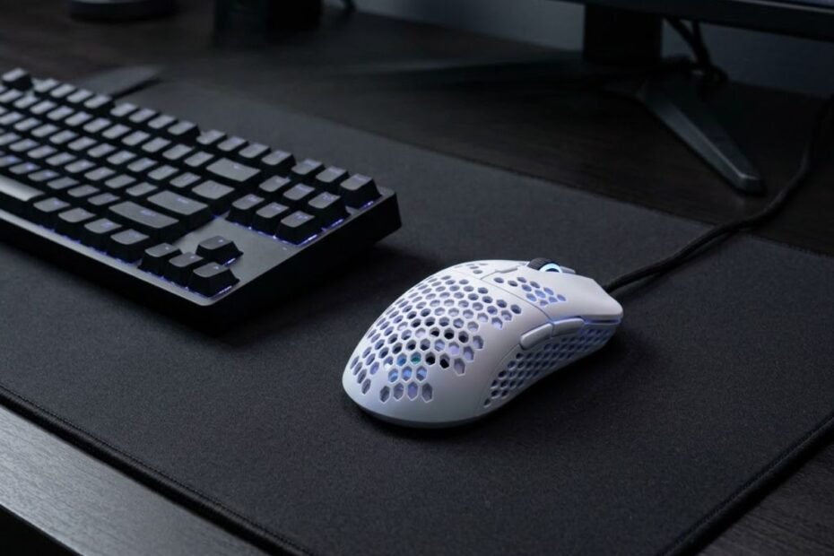 A lightweight gaming mouse resting on a large black mouse pad next to a mechanical keyboard on an FPS gaming desk