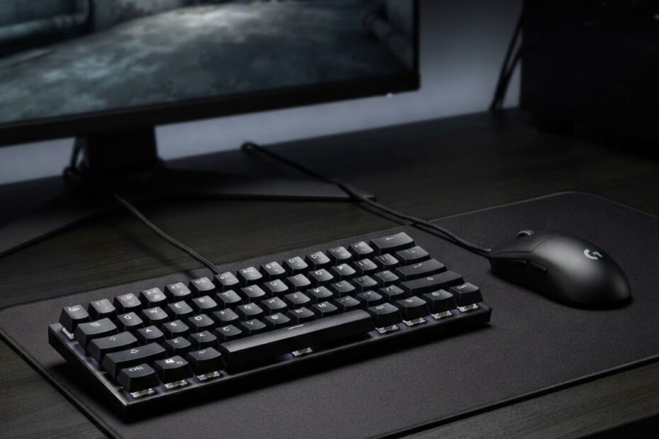 Gaming keyboard and mouse on a desk beside a monitor showing a competitive FPS game environment