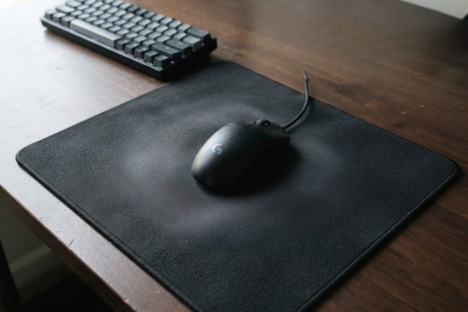 A black gaming mouse rests on a large cloth mouse pad with subtle surface wear visible across the active area.
